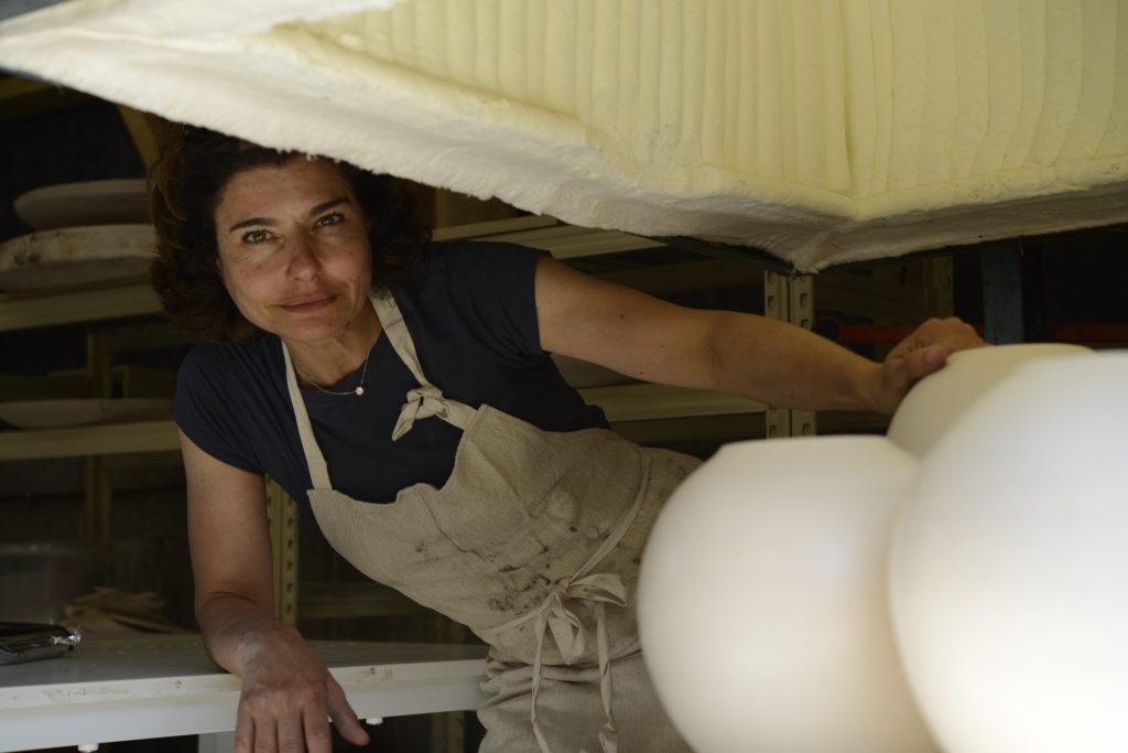 Portrait de Karen Swami posée avec ses pièces de céramique d'art, grands vases en poterie blanche, dans son atelier de poterie en France