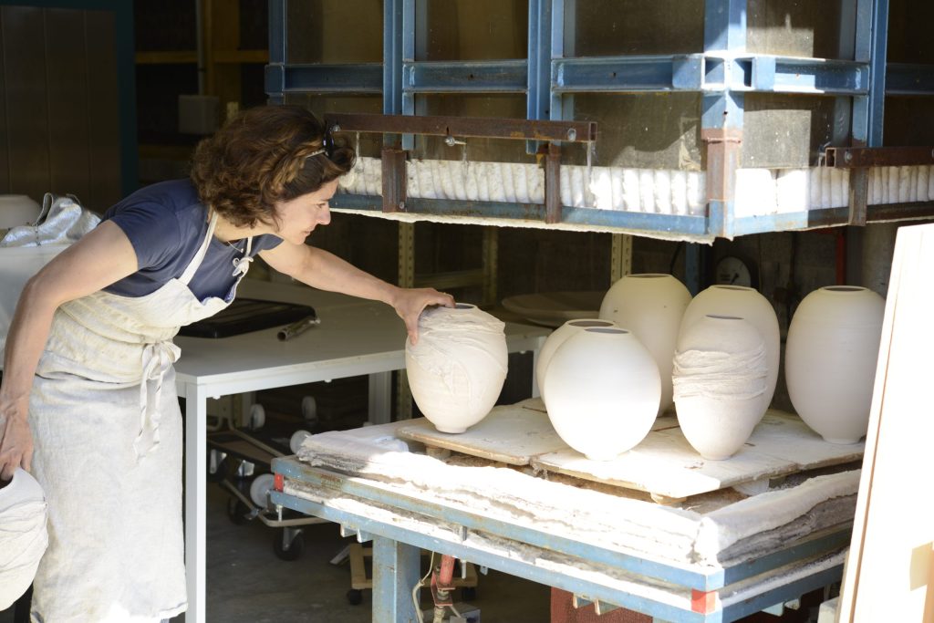 Portrait de Karen Swami devant ses 7 céramiques enfumées de couleur blanche, inspecter ses céramiques qui sortent de l'enfumage dans son atelier de céramique à Locquirec